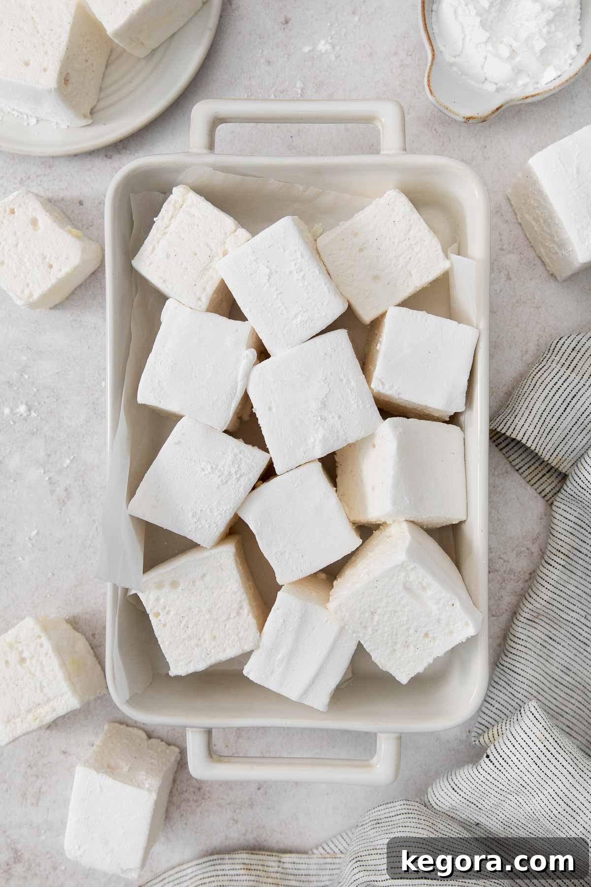 Pillowy Vanilla Bean Marshmallows 3 Pillowy soft homemade vanilla bean marshmallows, delicately dusted with powdered sugar and arranged invitingly in a baking dish, ready to be enjoyed.