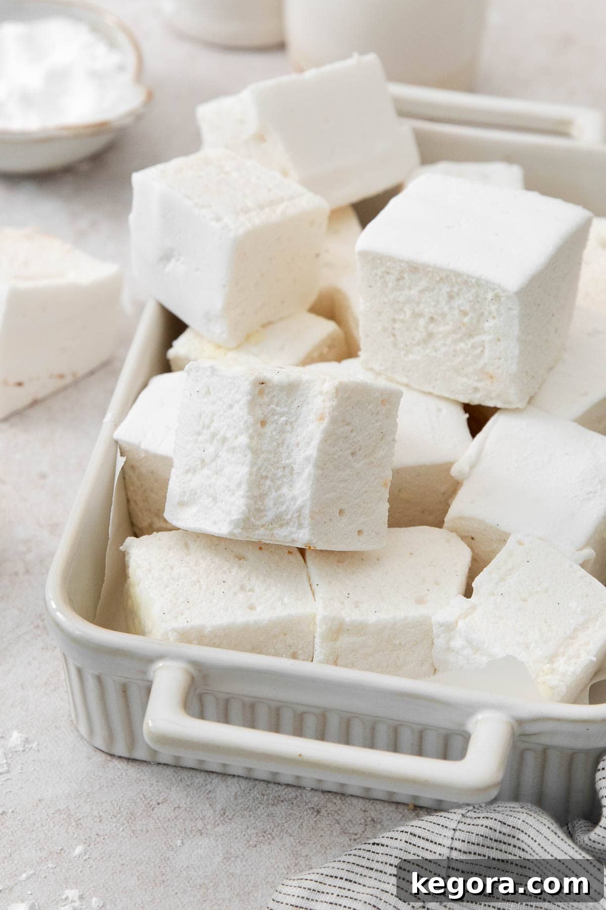 Pillowy Vanilla Bean Marshmallows 9 A delectable pile of homemade vanilla bean marshmallows, perfectly cut into squares and lightly dusted, beautifully showcasing their soft, airy texture and visible vanilla specks.