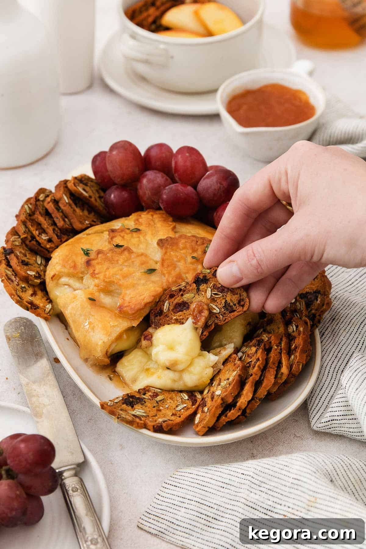 Decadent Gluten-Free Warm Brie 7 A hand dipping a cracker into gluten-free baked Brie.