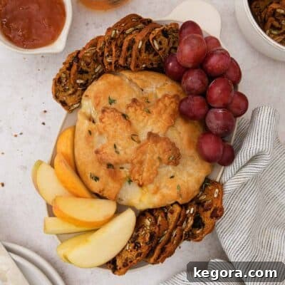 A square photo of gluten-free baked Brie on a platter with gluten-free crackers and grapes.
