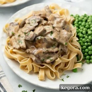 beef stroganoff on white plate topped with parsley and served with peas