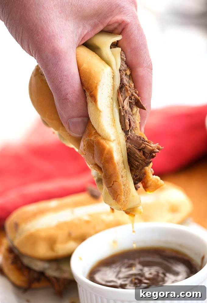 Instant Pot French Dip Perfection 7 Hand dipping French Dip Sandwich into a small white bowl of au jus, highlighting the irresistible dipping experience