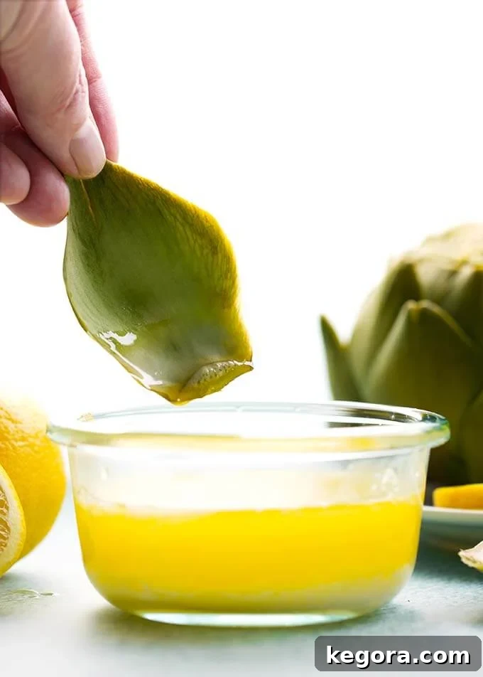 hand dipping part of artichoke into a small bowl of melted butter