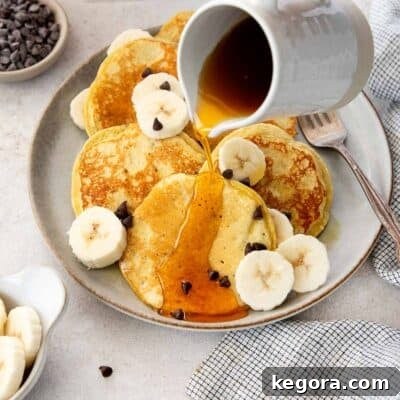 Gluten-free banana protein pancakes on a plate with maple syrup being poured over the top.