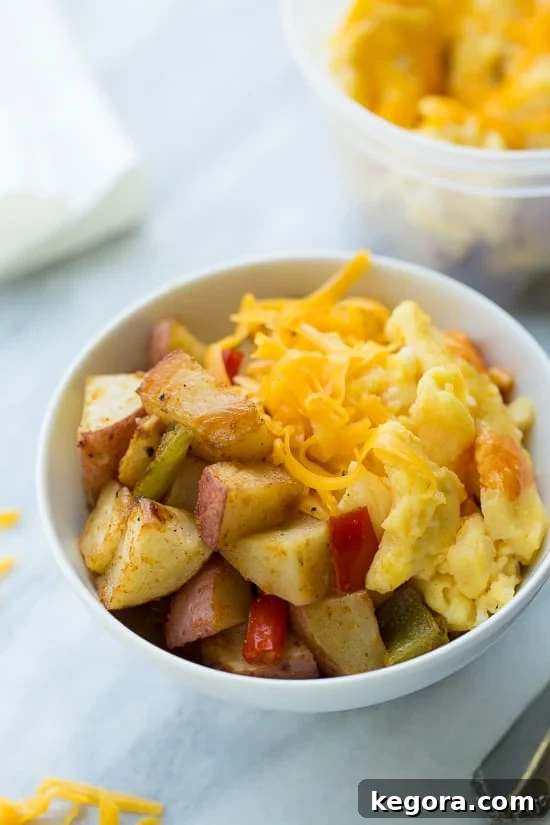 A vibrant breakfast bowl featuring golden roasted potatoes, fluffy scrambled eggs, and melted sharp cheddar cheese, garnished with fresh herbs, on a light marble background.