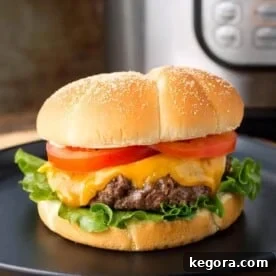 Hamburgers with cheese, lettuce, and tomato on a black plate in front of a pressure cooker