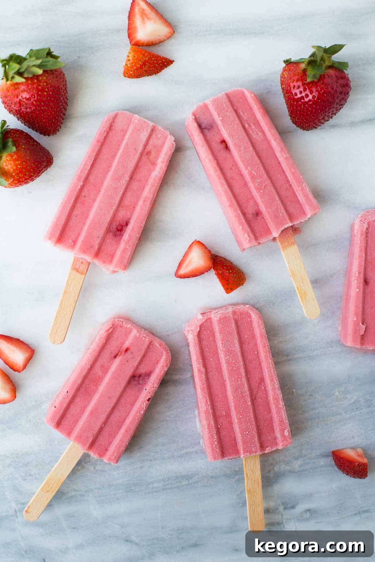 Strawberry Yogurt Popsicles Overhead shot of vibrant strawberry popsicles arranged artfully on a cool marble background, highlighting their refreshing appeal.