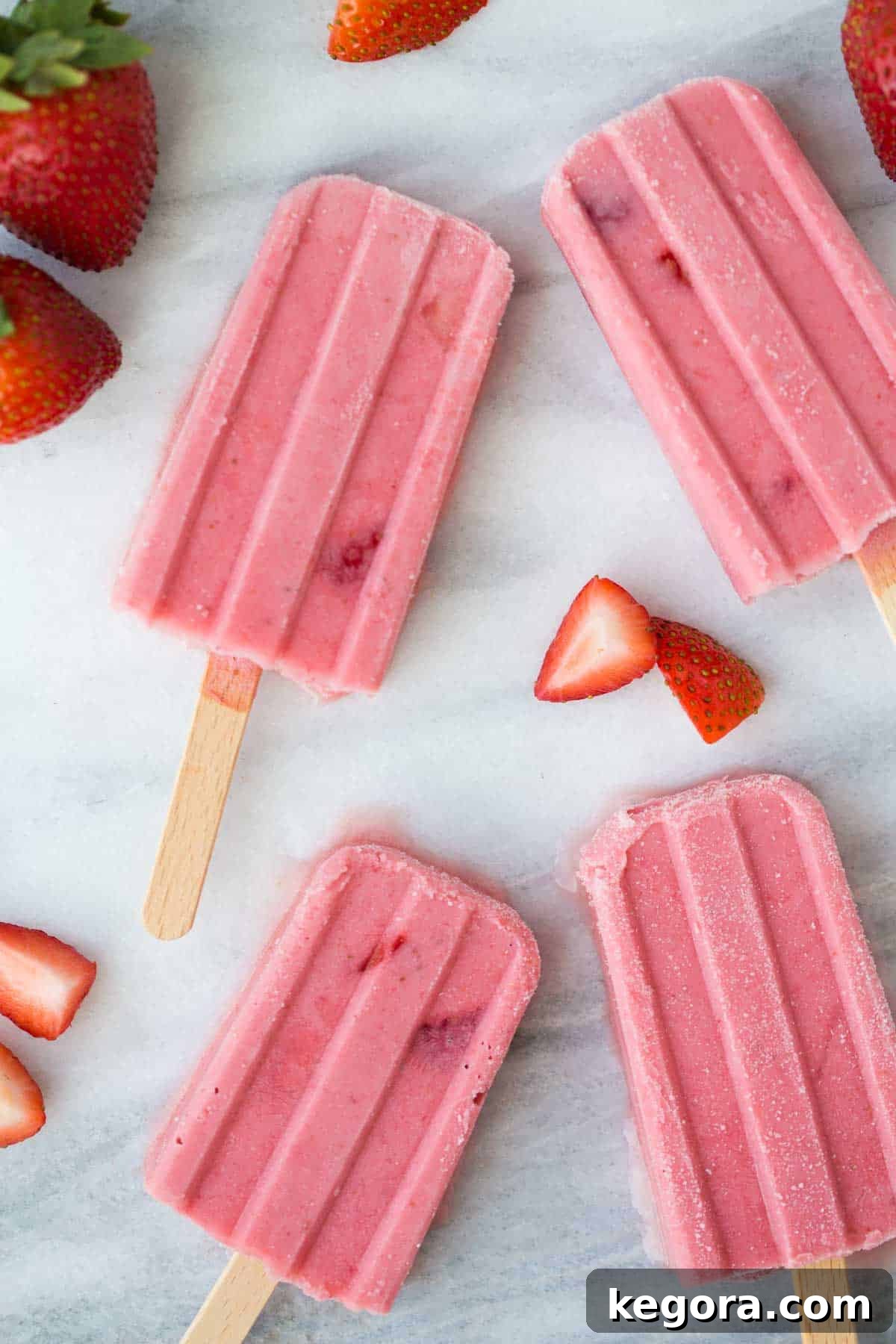 Fruit Popsicle Recipe Outcome A close-up shot of several vibrant strawberry fruit popsicles standing upright on a clean marble background, showcasing their fresh fruit chunks and creamy texture.
