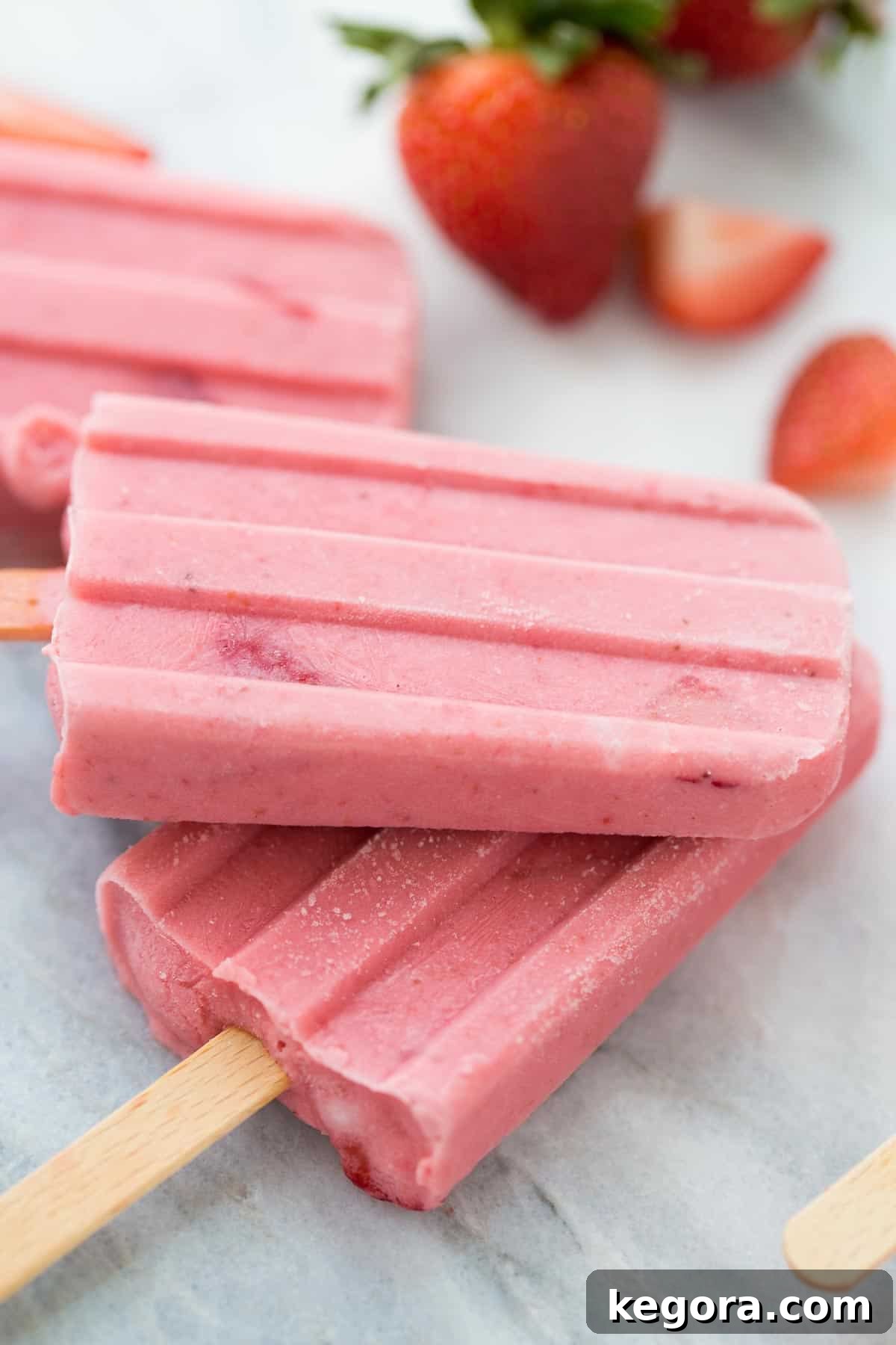 Fruit Popsicle Presentation Two vibrant strawberry fruit popsicles neatly stacked on top of each other on a sleek marble background, emphasizing their fresh and inviting appearance.