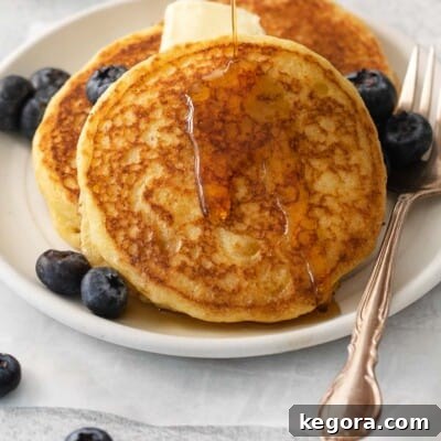 Cornmeal pancakes on a plate with blueberries and a pat of butter on top
