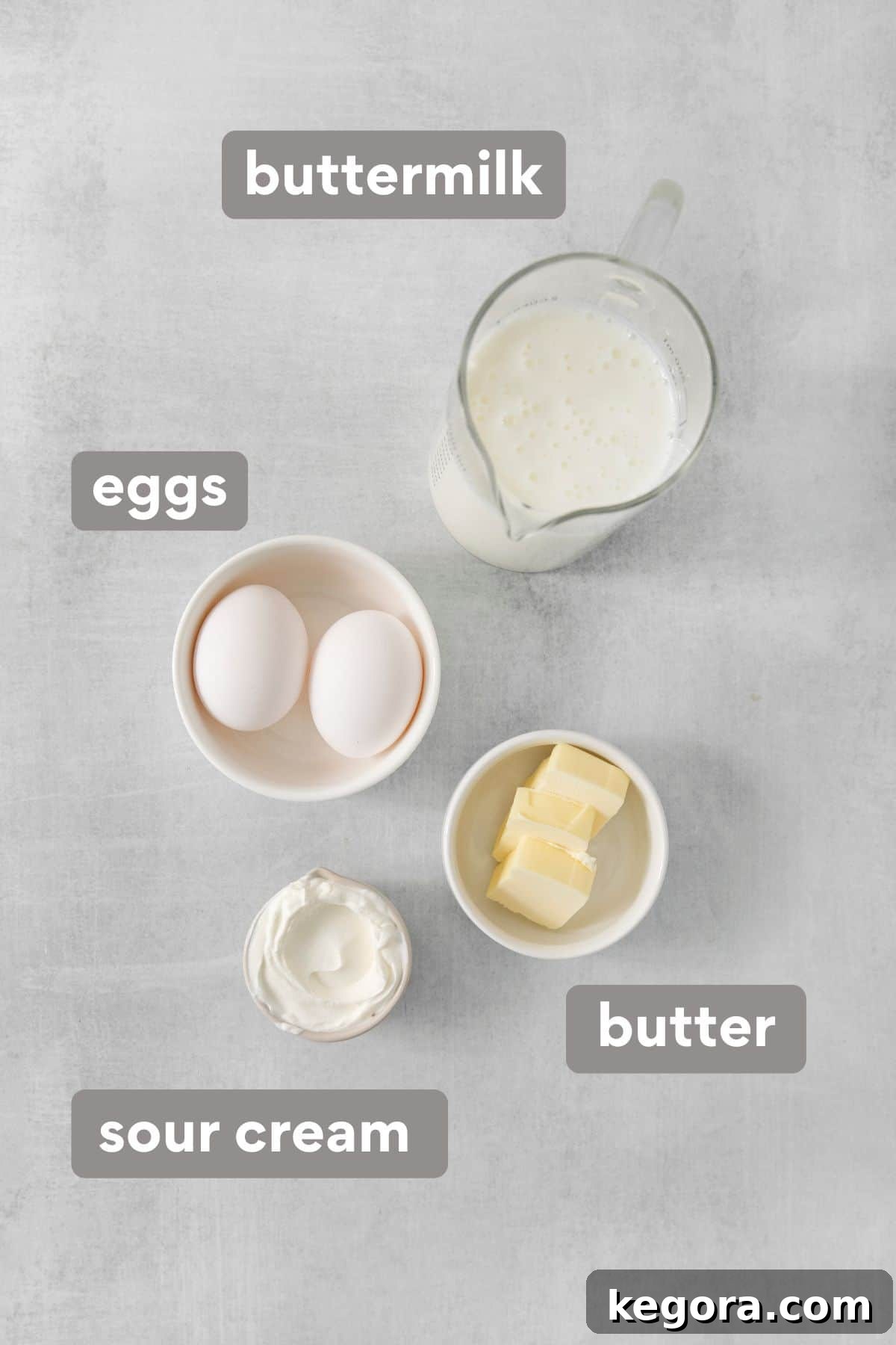 Silky Corn Cakes 4 A collection of wet ingredients for cornmeal pancakes, including buttermilk, sour cream, eggs, and melted butter, arranged on a kitchen countertop.