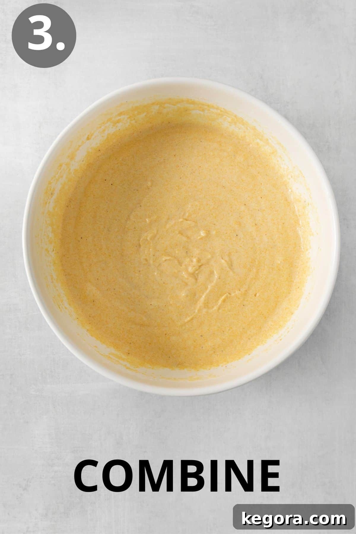 Silky Corn Cakes 7 Wet and dry ingredients for cornmeal pancakes are gently combined in a mixing bowl, forming a slightly lumpy batter ready for resting.