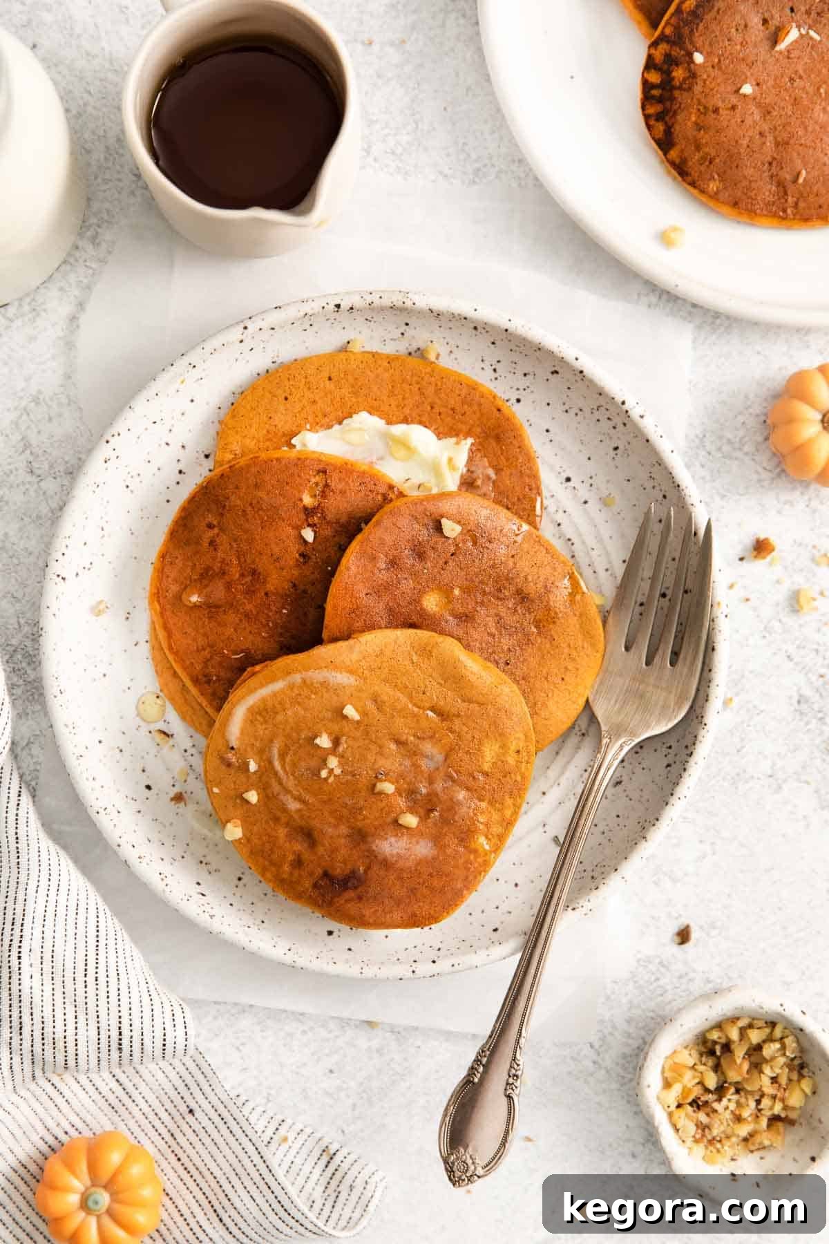 Pumpkin protein pancakes piled on a plate with a pat of butter on top and a fork next to it, ready to be enjoyed.