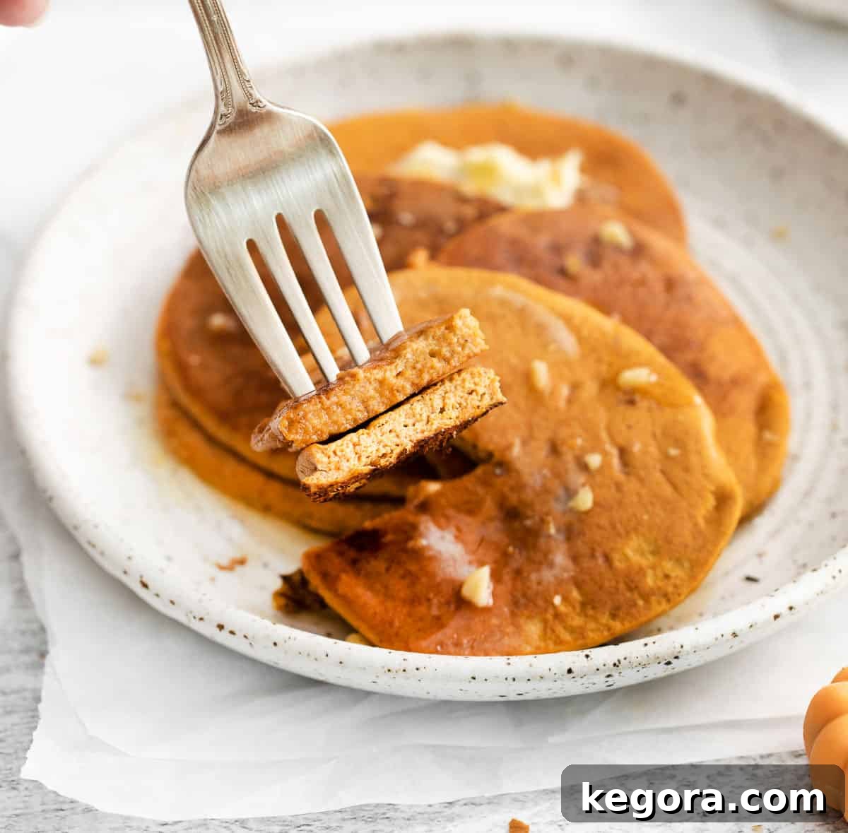 A fork picking up a bite of pumpkin pancakes from a plate, highlighting their fluffy texture.