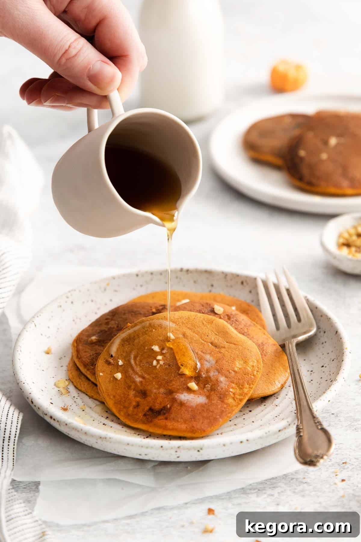 Pumpkin pancakes on a plate with syrup being poured over them.
