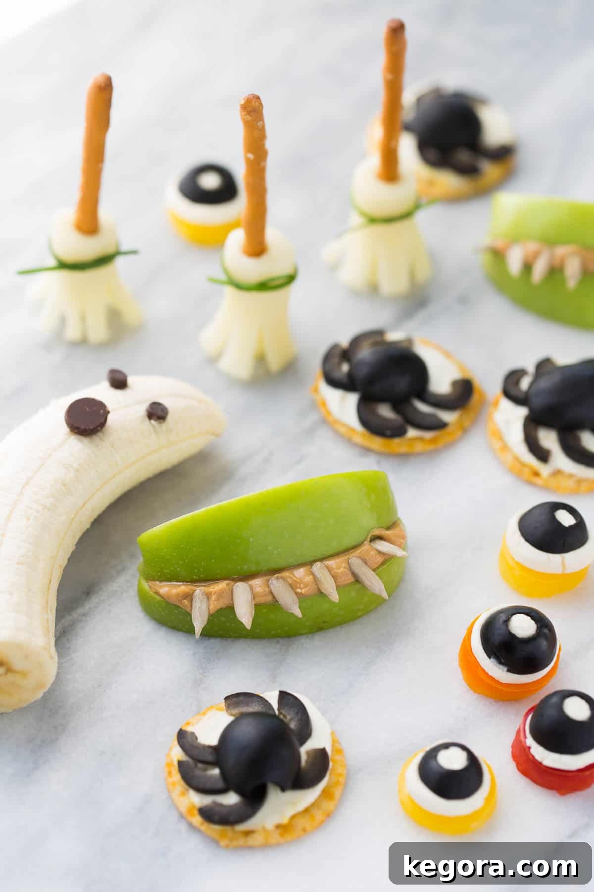 Spooktacularly Healthy Treats 2 A vibrant display of healthy Halloween snacks on a white marble background, featuring monster eyes, spider bites, and boo-nanas.