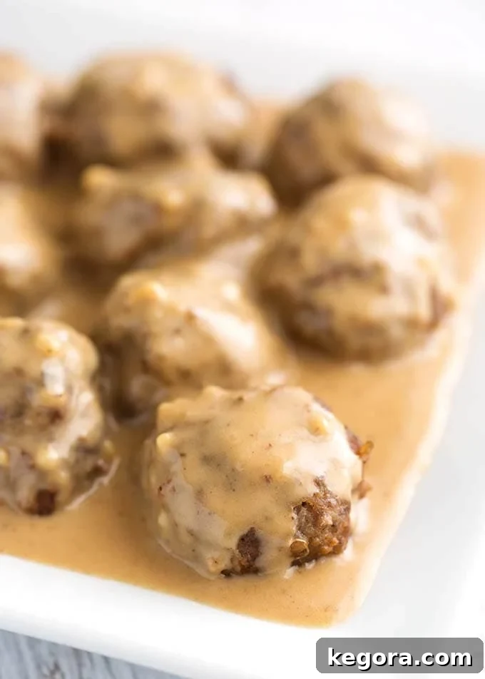 Creamy Instant Pot Swedish Meatballs 2 Closeup of Instant Pot Swedish Meatballs on a white plate, garnished with fresh parsley. The meatballs are covered in a rich, creamy brown sauce.