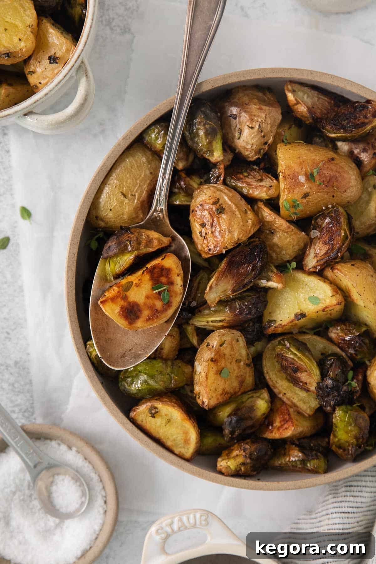 a spoon in a bowl of roasted potatoes and brussel sprouts 