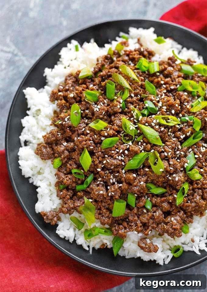 Korean Ground Beef over rice on a black plate with chopsticks, garnished with green onions and sesame seeds