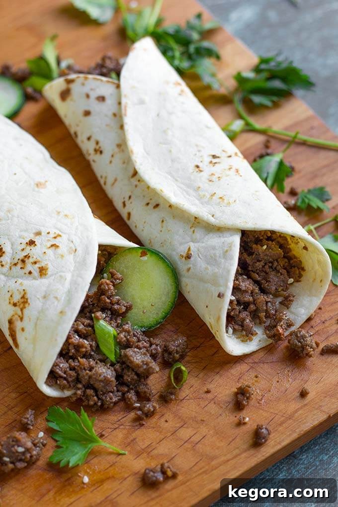 Korean Ground Beef rolled in flour tortillas on a wooden board, garnished with green onions