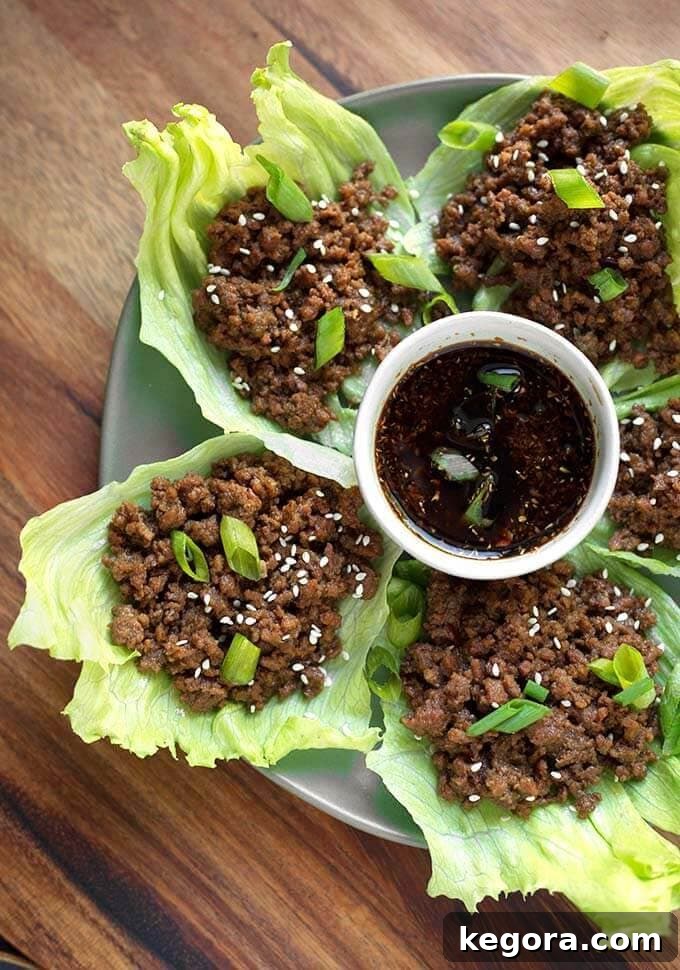 Korean Ground Beef served on lettuce leaves with a small bowl of dipping sauce in the center, garnished with green onions and sesame seeds