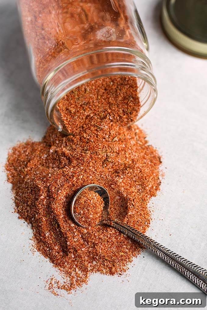 Rotisserie Chicken Spice Rub spilling out of a small glass jar, showcasing its rich color and texture