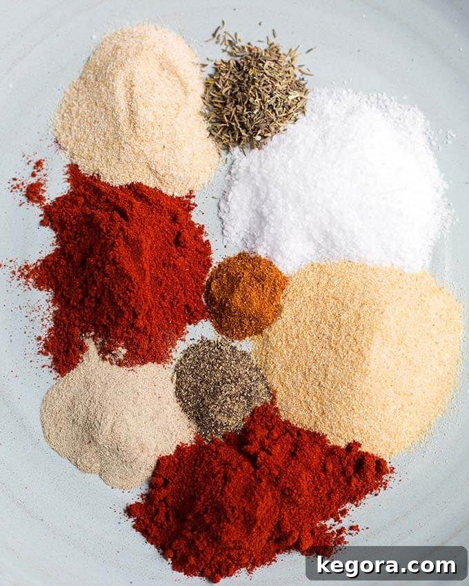 A collection of Rotisserie Chicken Spice Rub ingredients laid out on a clean white background, highlighting the vibrant colors of individual spices