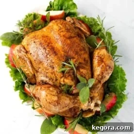Top view of a cooked Whole Chicken on a white plate with green herbs, leafy vegetables, and apple slices