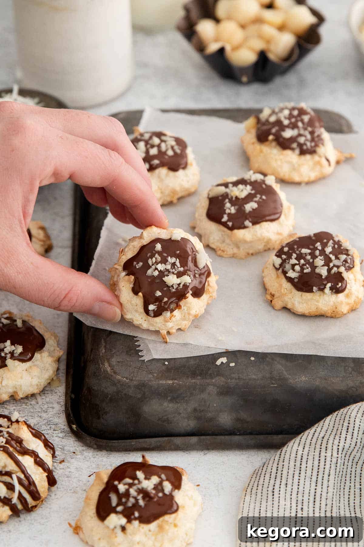 Ethereal Coconut Clouds Gluten Free 8 chocolate coconut cloud cookies on parchment paper with a hand holding up one cookie.