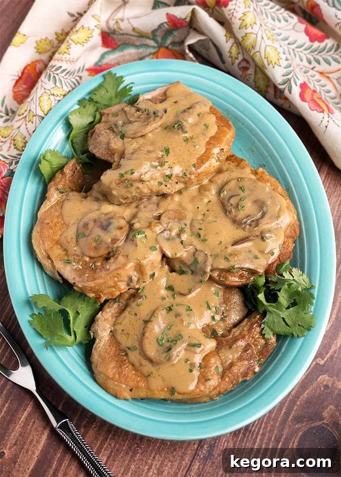 Top view of perfectly cooked Instant Pot Pork Chops with Mushroom Gravy served on a blue plate, garnished with fresh herbs