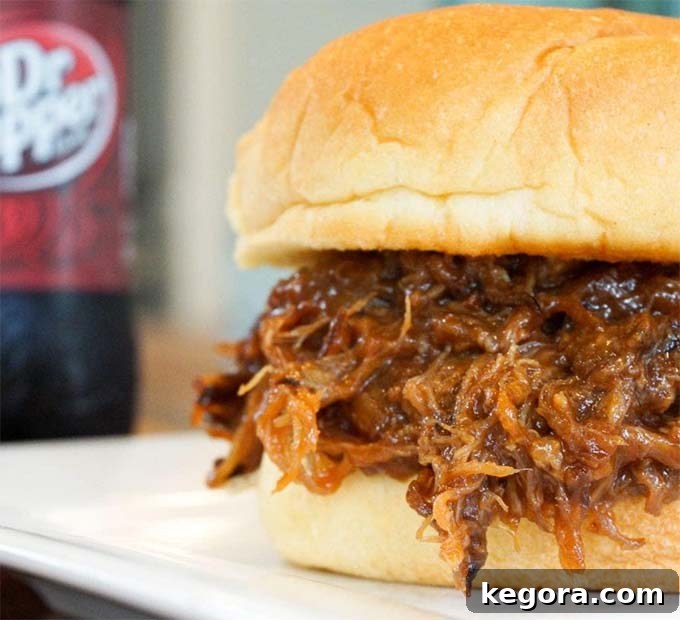Dr Pepper pulled pork piled high on a hamburger bun, served on a white plate, showcasing its tender texture.