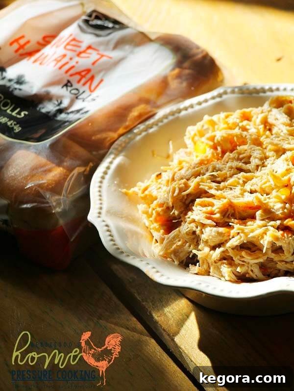 Weight Watchers shredded spicy mango chicken in a white bowl, accompanied by a package of sweet Hawaiian rolls, suggesting delicious sandwich possibilities.