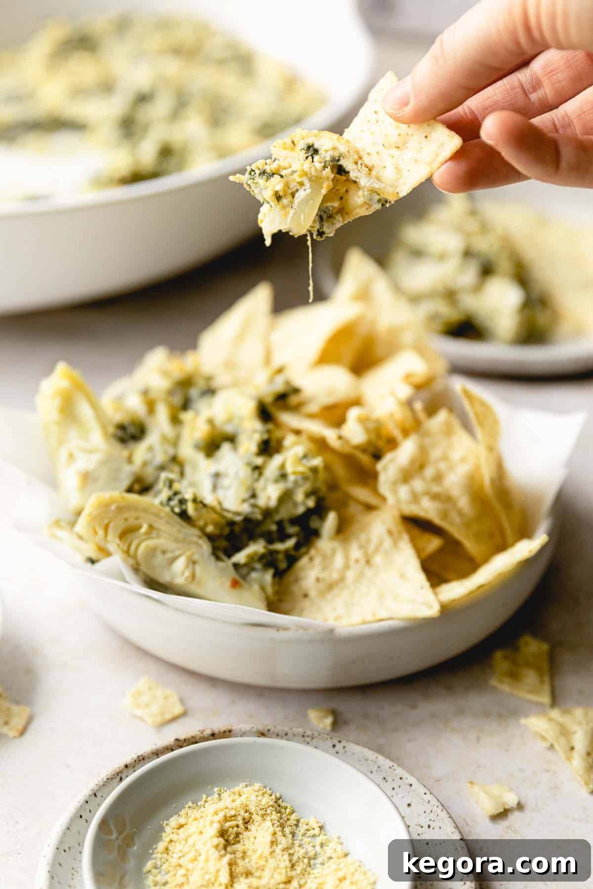 Creamy Spinach Artichoke Dip Without Dairy 9 chip scooping up a bite of the dip with bowl of chips and dip in the background