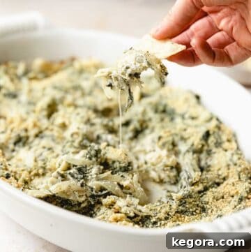 spinach artichoke dip in baking dish with chip for dipping