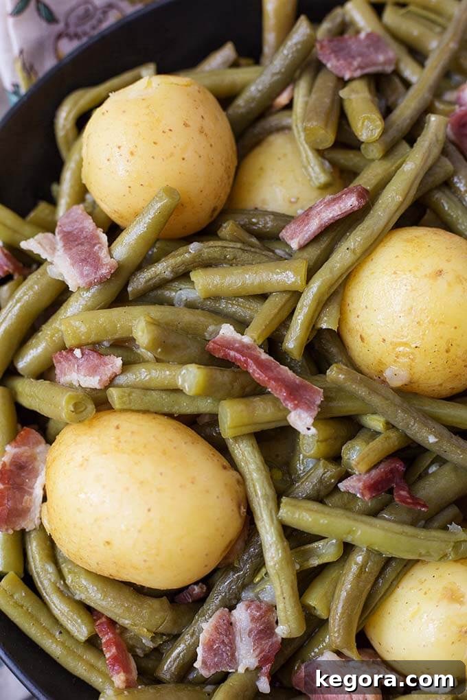 A close-up view of the tender Instant Pot Green Beans with New Potatoes and Bacon in a black bowl, highlighting the rich broth and the perfectly cooked ingredients, a comforting meal.