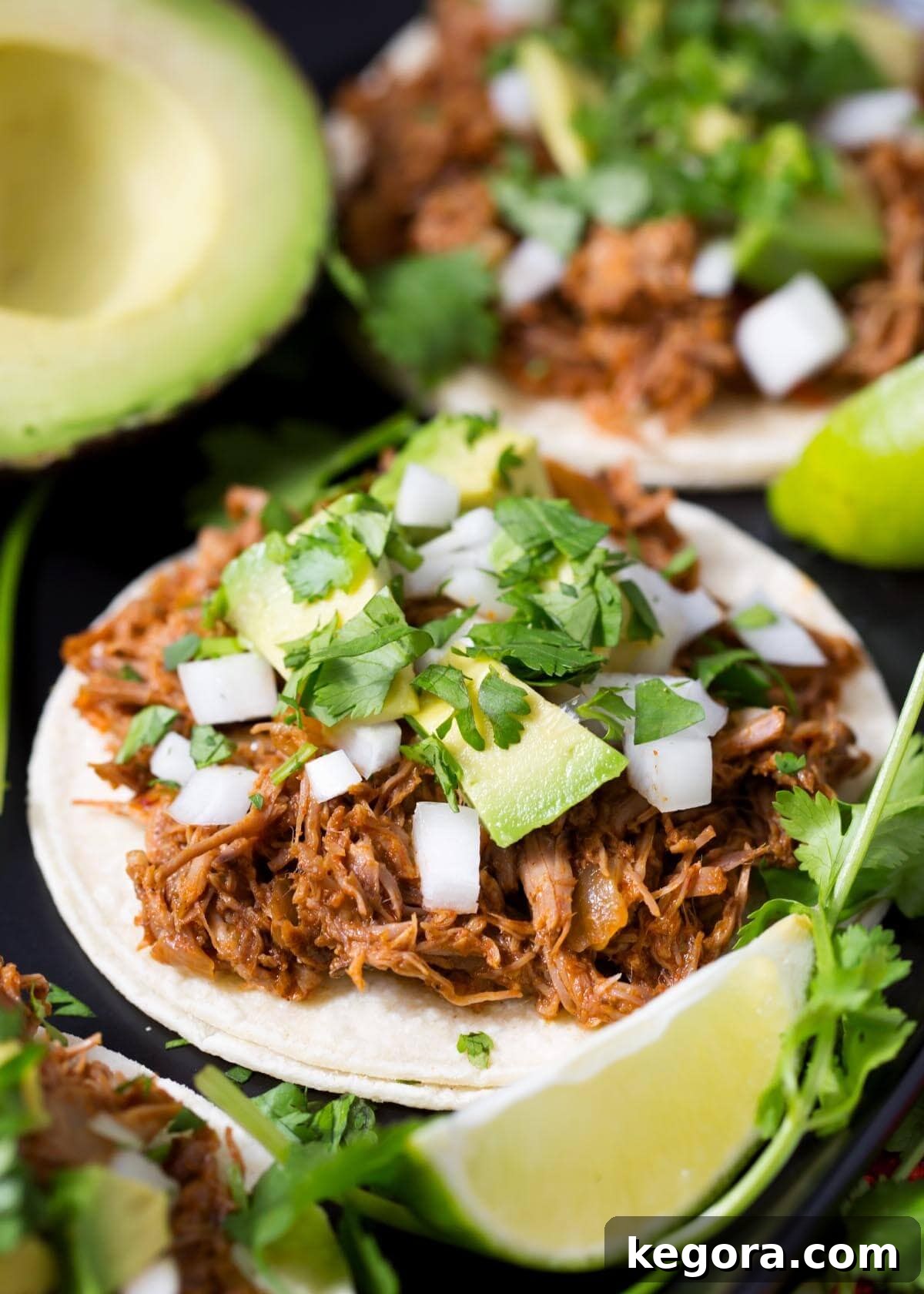 Slow Cooker Barbacoa Beef on a tortilla with garnishes, showcasing its tender texture and rich color.