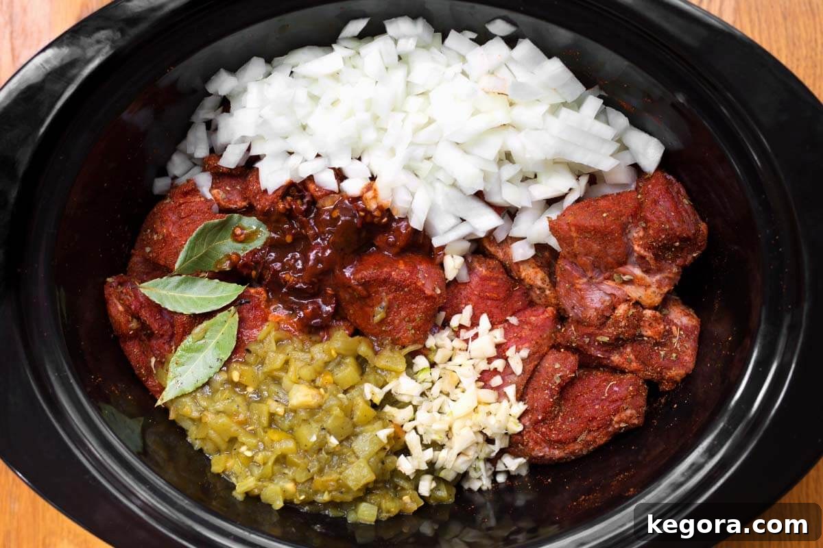 Slow Cooker Barbacoa Beef ingredients artfully arranged in a crockpot before cooking, highlighting fresh aromatics and spices.