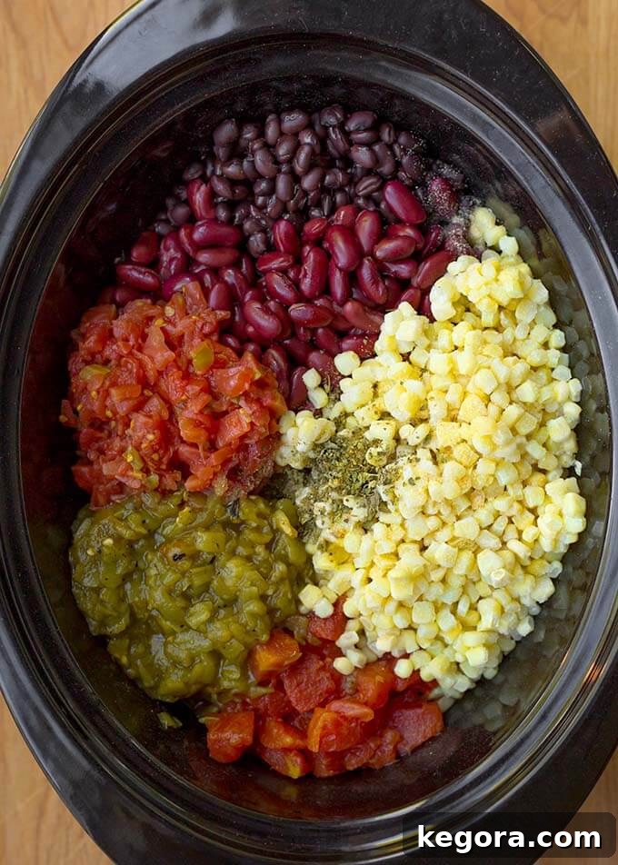 Various ingredients for a hearty Slow Cooker Taco Soup, including canned beans, corn, tomatoes, and spices, gathered in a black slow cooker before cooking.