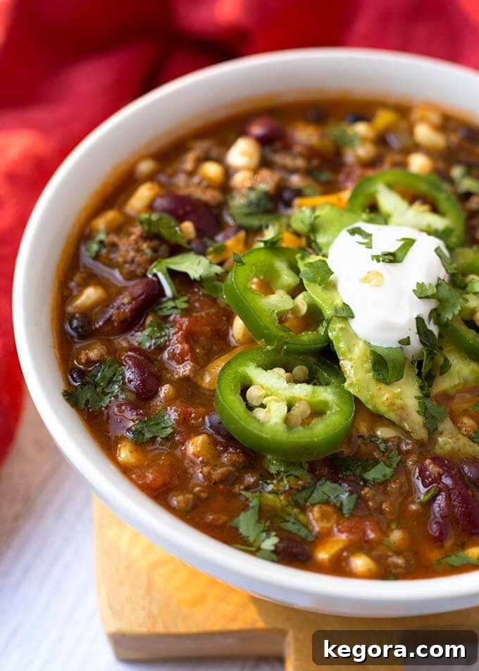 A close-up view of a white bowl filled with Slow Cooker Taco Soup, generously topped with vibrant sliced jalapeños and a swirl of creamy sour cream, showcasing its appetizing appeal.