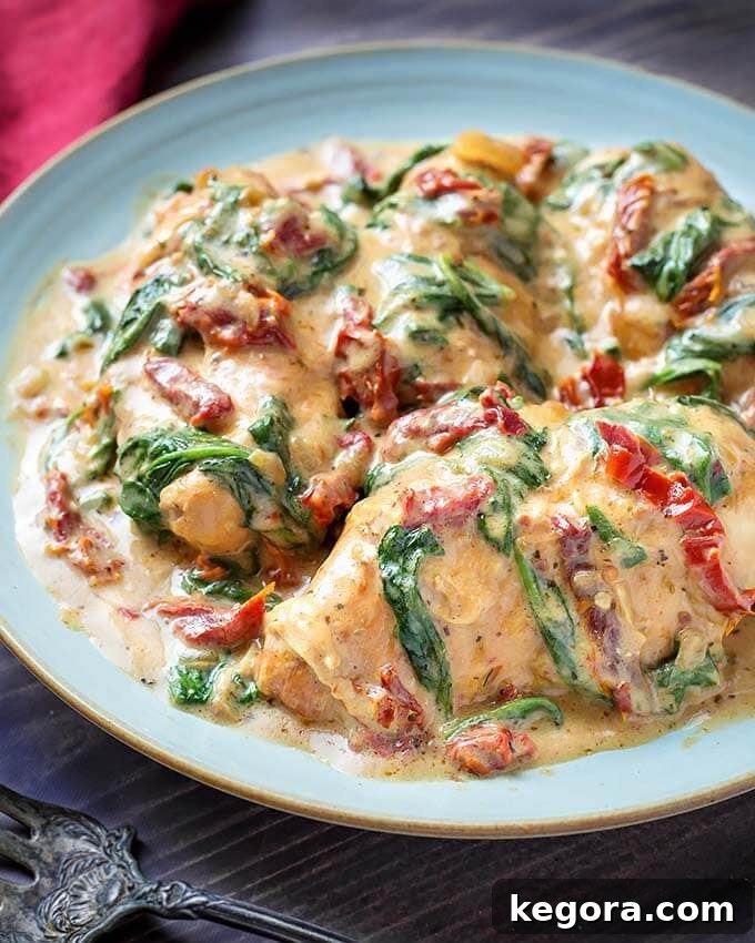Creamy Slow Cooker Tuscan Chicken 2 Creamy Tuscan Chicken on a light blue plate, garnished with fresh herbs