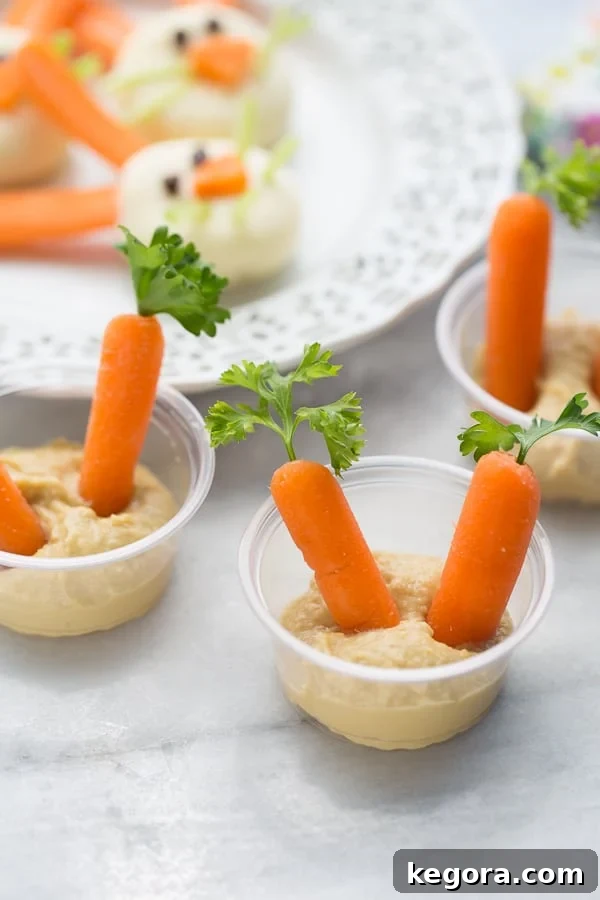 Wholesome Easter Snacking Ideas 3 Individual serving cups filled with creamy hummus, topped with vibrant baby carrots and fresh parsley, resembling tiny garden plots. Perfect healthy Easter snack for kids.