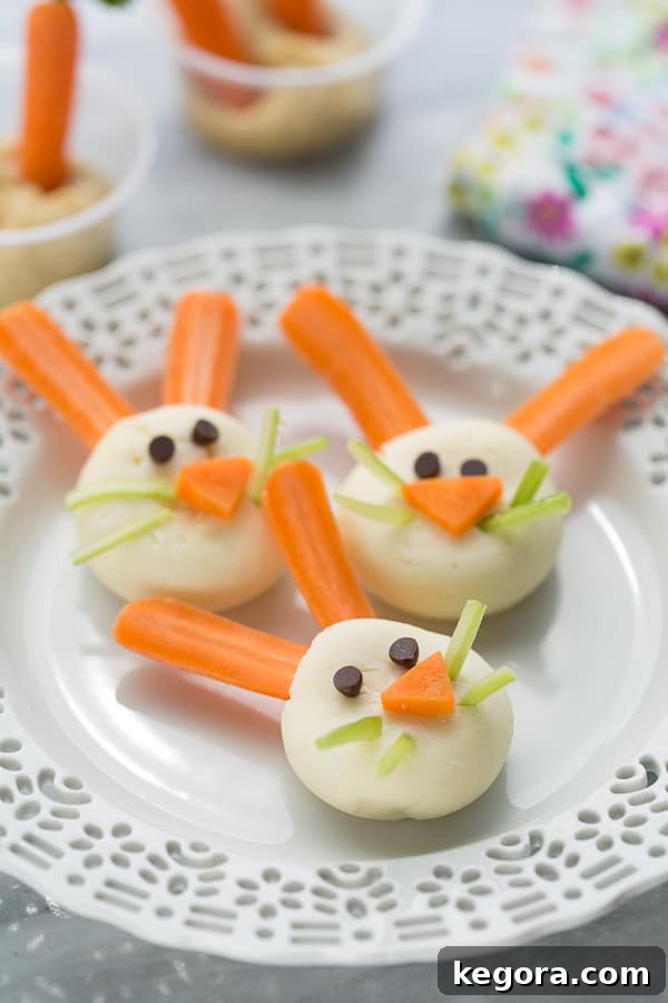 Wholesome Easter Snacking Ideas 4 Close-up of a cute bunny face snack on a white plate, made from a mini circle cheese with carrot ears and nose, celery whiskers, and mini chocolate chip eyes. A perfect healthy Easter snack.