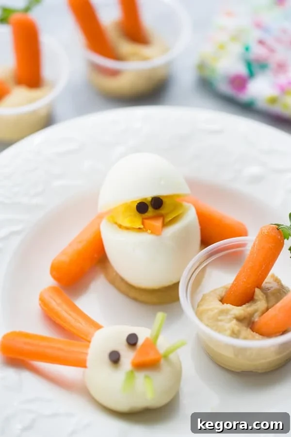 Wholesome Easter Snacking Ideas 5 A festive white plate featuring three healthy Easter snacks: a cute hard-boiled egg chick with chocolate chip eyes and carrot beak, a hummus cup with carrots and parsley, and a bunny cheese face.