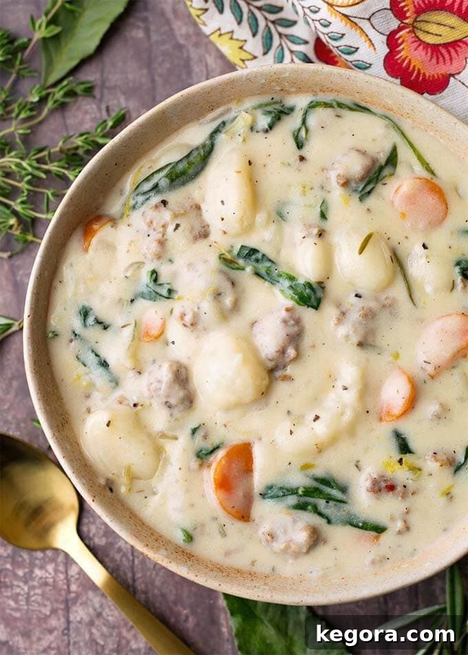 Creamy Sausage Gnocchi Soup in a beige bowl next to a golden spoon