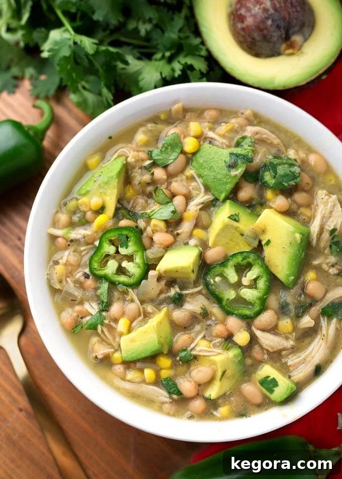White Chicken Chili topped with diced avocado and fresh jalapeno slices in a white bowl on a wooden board