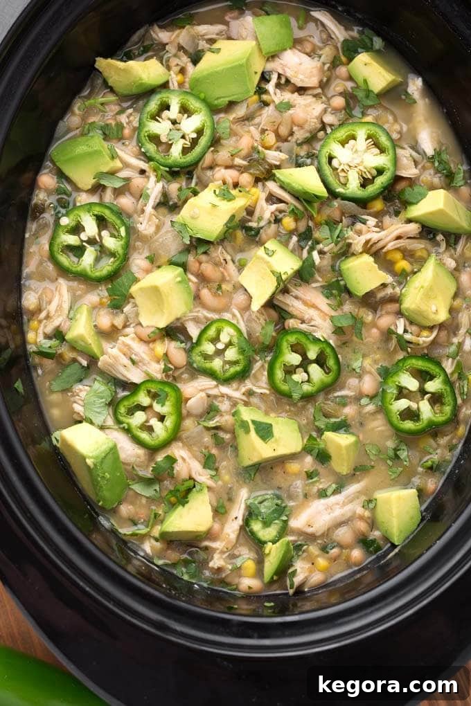 Closeup of White Chicken Chili topped with diced avocado and fresh jalapeno slices in a black slow cooker