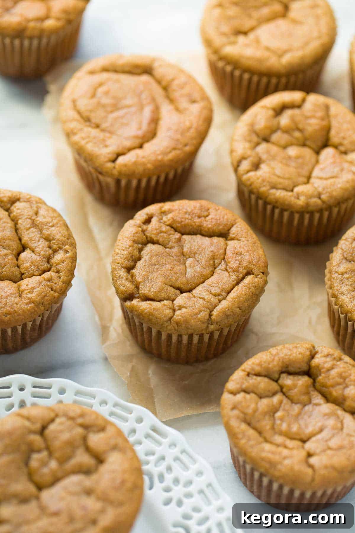 Tropical Banana Coconut Muffins 5 Freshly baked coconut flour banana muffins displayed on a white plate, with a subtle marble background and a piece of brown parchment paper, highlighting their golden perfection and inviting texture.