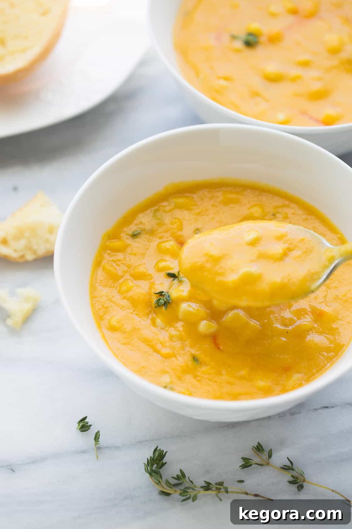 A spoon dipping into a bowl of creamy corn soup, showcasing its rich texture and inviting warmth.