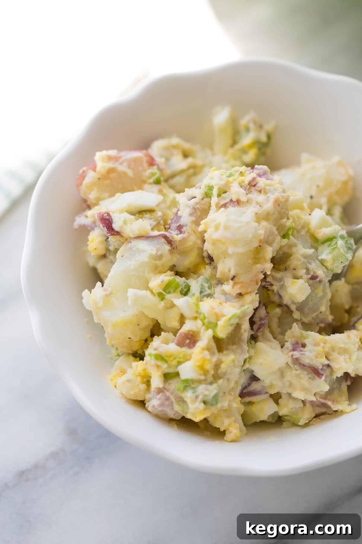 Potato Salad Recipe A large white bowl of creamy potato salad, garnished with fresh green onions, ready to be served at a BBQ.
