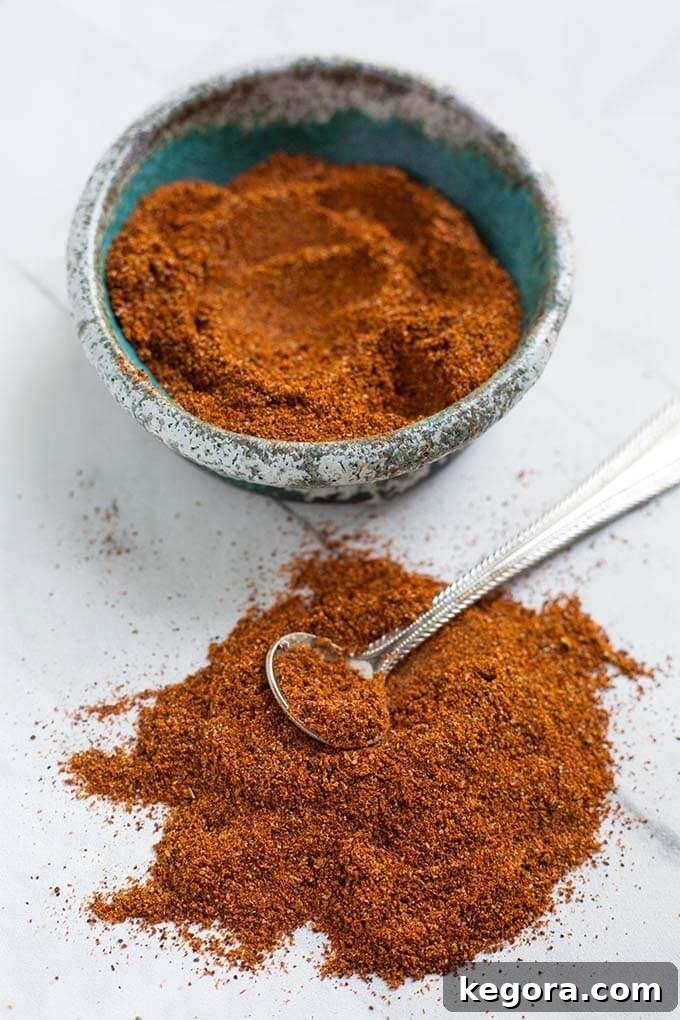 Homemade Fajita Seasoning in a turquoise stoneware bowl next to a small pile of seasoning with a silver teaspoon on a white background